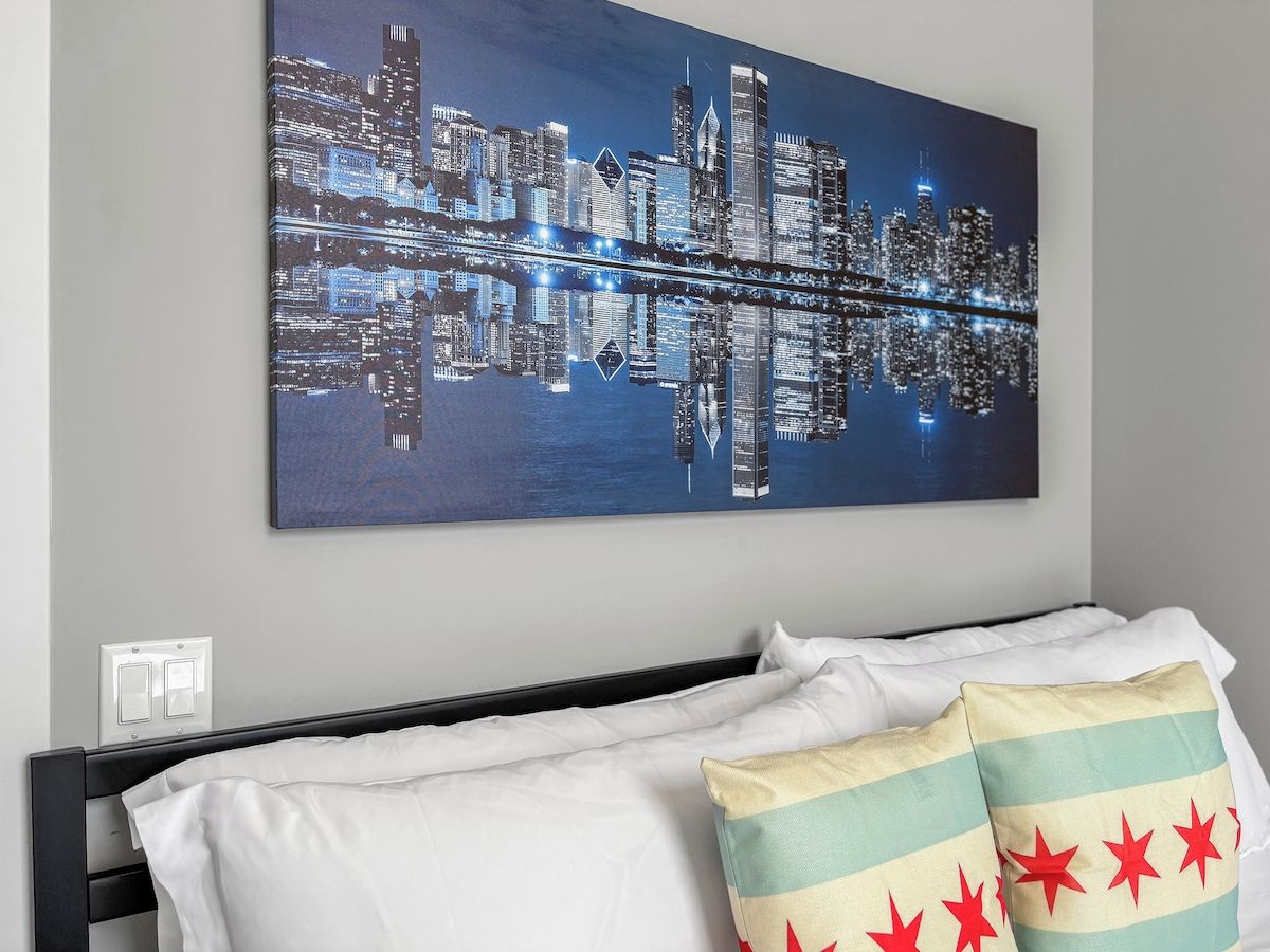 Ein Hotelzimmer mit einem Bett, weißer Bettwäsche und einem Stadtbild an der Wand.