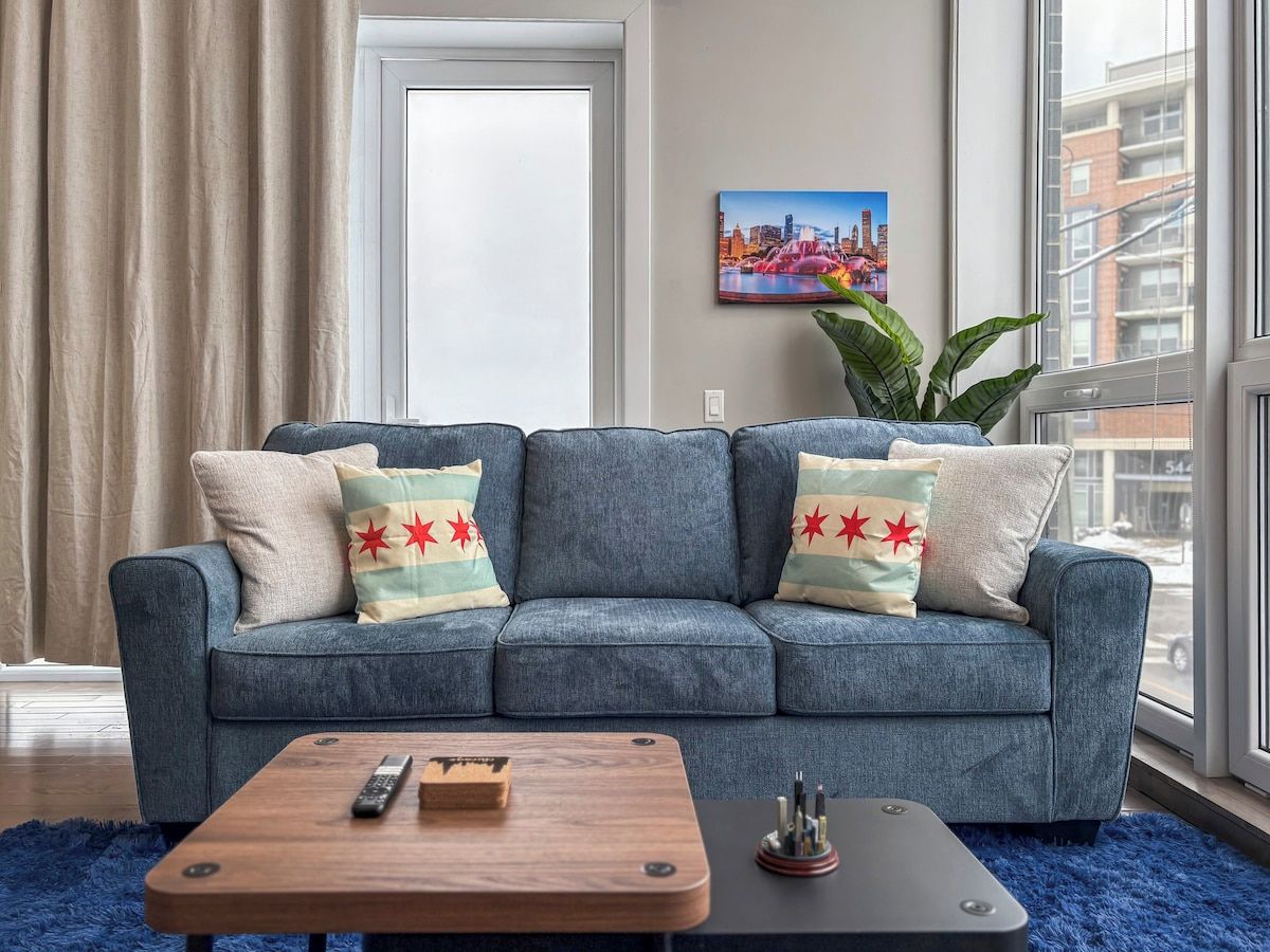 A living room with a blue sofa, a wooden coffee table, and a cityscape painting on the wall.
