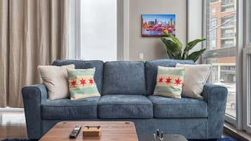 A living room with a blue sofa, a wooden coffee table, and a cityscape painting on the wall.