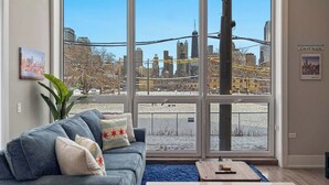Un salón con un ventanal grande, un sofá, una mesa de centro y vistas a la ciudad.
