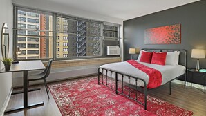 A modern hotel room with a large bed, a desk, and a view of the cityscape through floor-to-ceiling windows. - Sunlit 2BR - Fully Furnished & Spacious Apartment (Chicago)