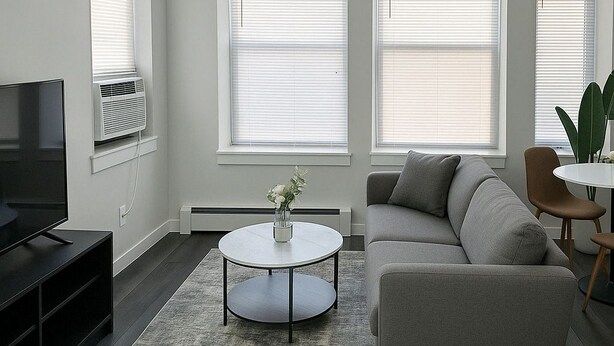 A modern living room with a grey sofa, a round coffee table, and a TV on a stand. - Hyde Park 1BR w/ Charm (Chicago)