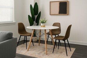 Un coin repas avec une table ronde, deux chaises, une plante en pot et une œuvre d’art encadrée accrochée au mur.
