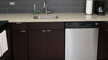 Cozinha moderna com armários escuros, lava-louças de aço inoxidável, pia e cafeteira.