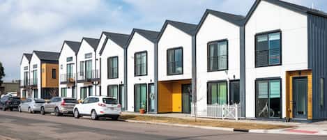 A row of modern townhouses with large windows, a gated driveway, and a clear sky.