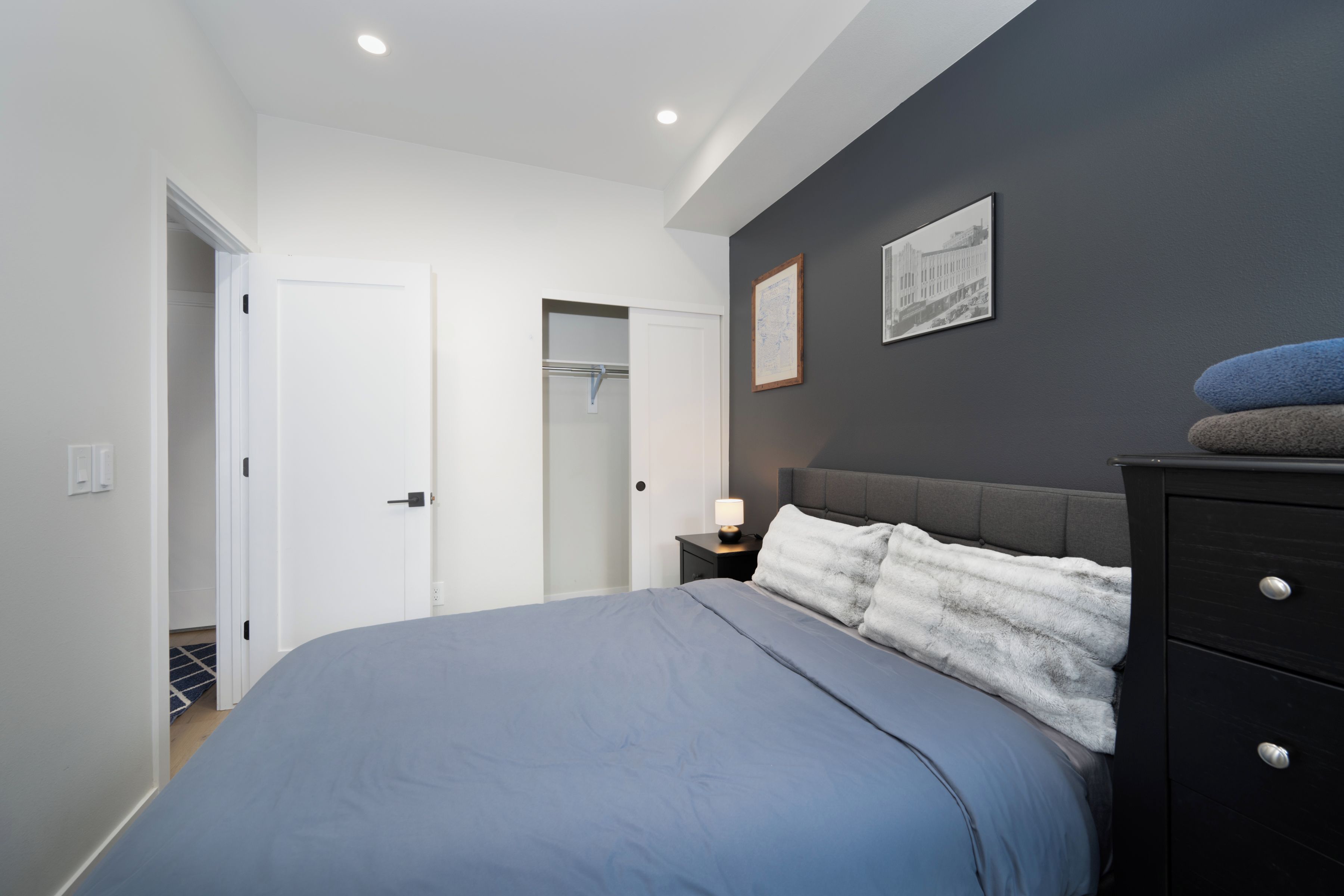 Un dormitorio con cama, mesita de noche, cómoda, una puerta y una pared con dos cuadros.
