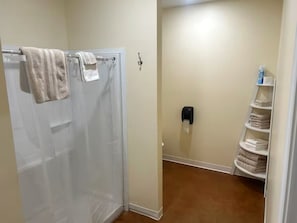Ein Badezimmer mit Dusche, Handtuchhalter, Seifenspender und Ablage mit gefalteten Handtüchern.