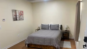 Un dormitorio con cama, mesitas de noche, lámpara, un cuadro y una puerta.