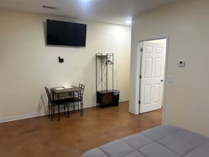 A room with a bed, a dining table with chairs, a TV mounted on the wall, and a door.