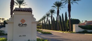 A sign for La Quinta Resort & Club with a date of 1926, surrounded by a row of tall palm trees and a paved pathway.