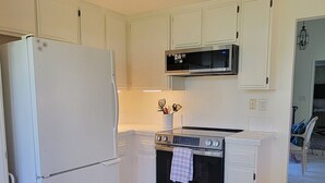 A kitchen with white cabinetry, a stainless steel oven, a microwave, and a chandelier.