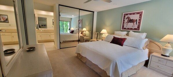 Een slaapkamer met een groot bed, nachtkastjes, een spiegel en uitzicht op de badkamer.