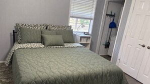 Ein Bett mit einer gesteppten grünen Bettdecke, einem gemusterten Kopfteil und einem Nachttisch mit einer Lampe.