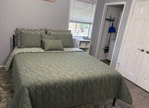 Uma cama com colcha verde acolchoada, cabeceira estampada e mesa de cabeceira com abajur.