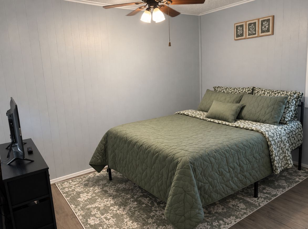 A bedroom with a bed, a ceiling fan, a desk, and a rug.