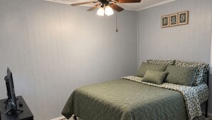 Ein Schlafzimmer mit einem Bett, einem Deckenventilator, einem Schreibtisch und einem Teppich.