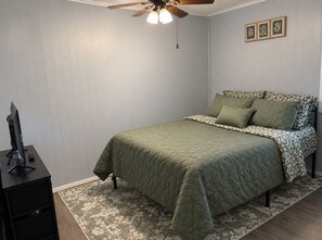 Um quarto com cama, ventilador de teto, escrivaninha e tapete.