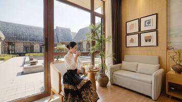 Ein Zimmer mit großen Fenstern, einem Sofa, einem Tisch mit Teeservice und gerahmten Kunstwerken an der Wand.