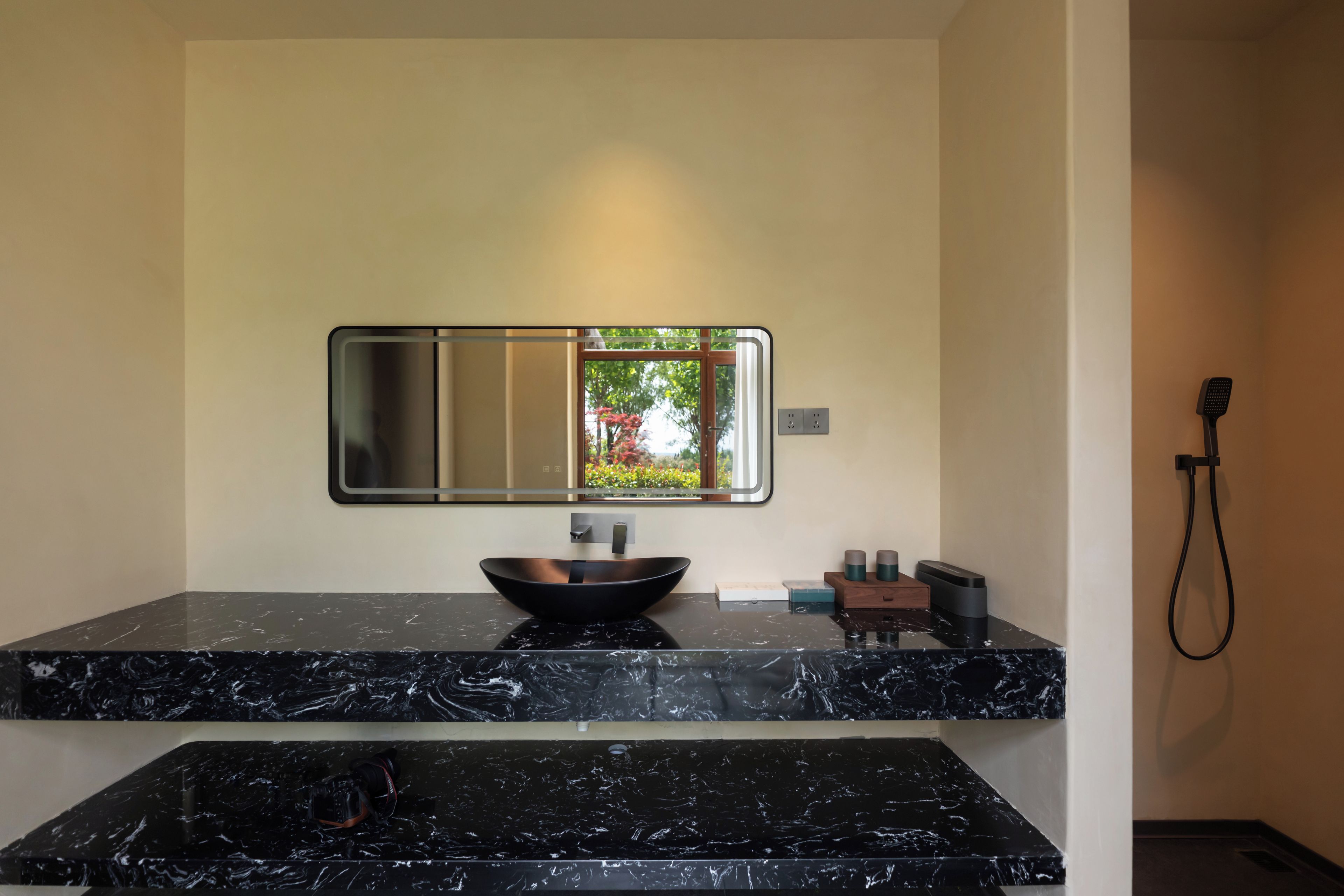 A bathroom with a black marble countertop, a vessel sink, a mirror, and a handheld showerhead.