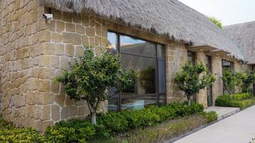 A stone building with a thatched roof, large windows, and small trees in the foreground.