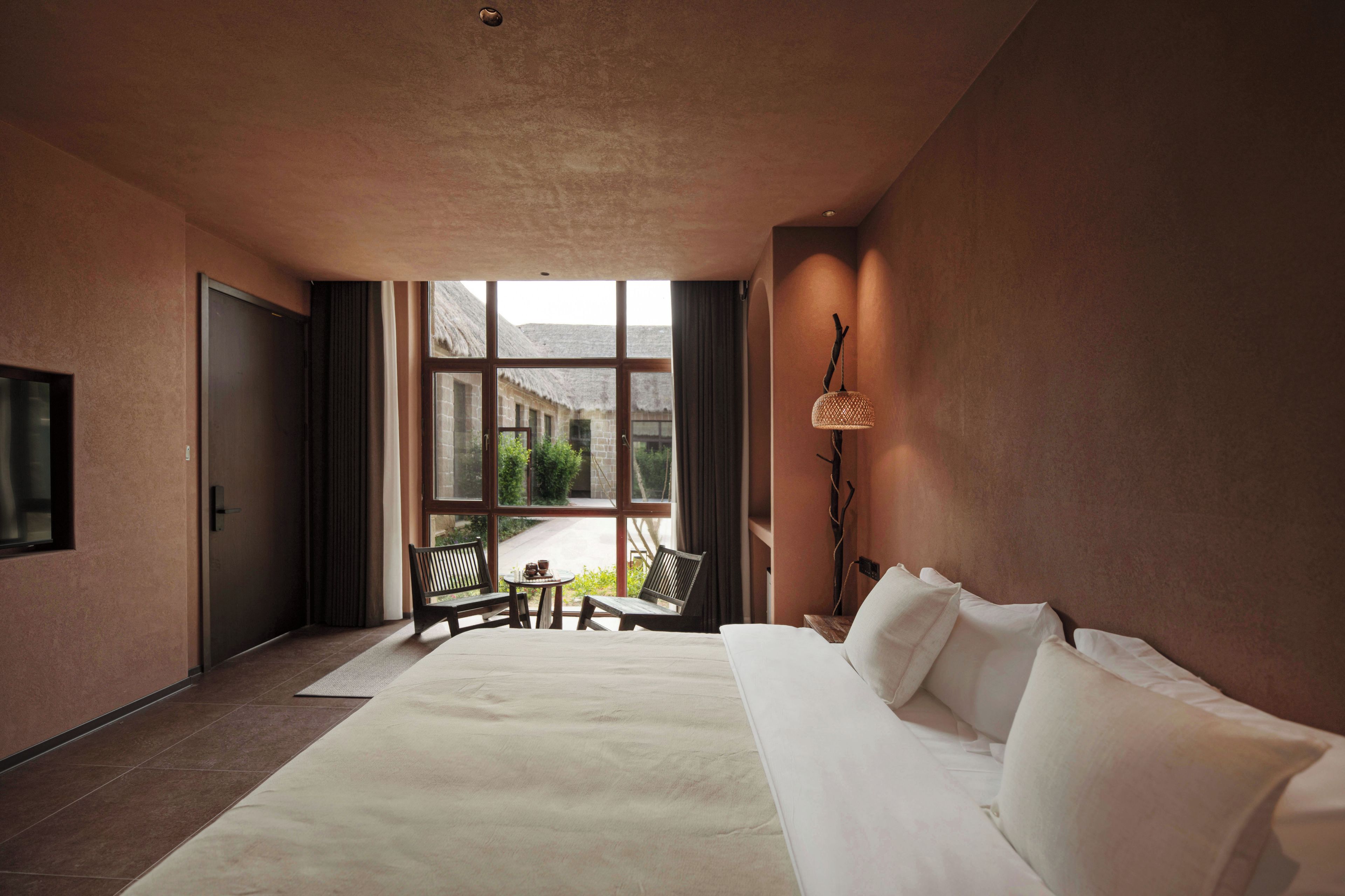Habitación de hotel con una cama grande, una zona de estar con mesa y sillas, y vistas a través del ventanal.