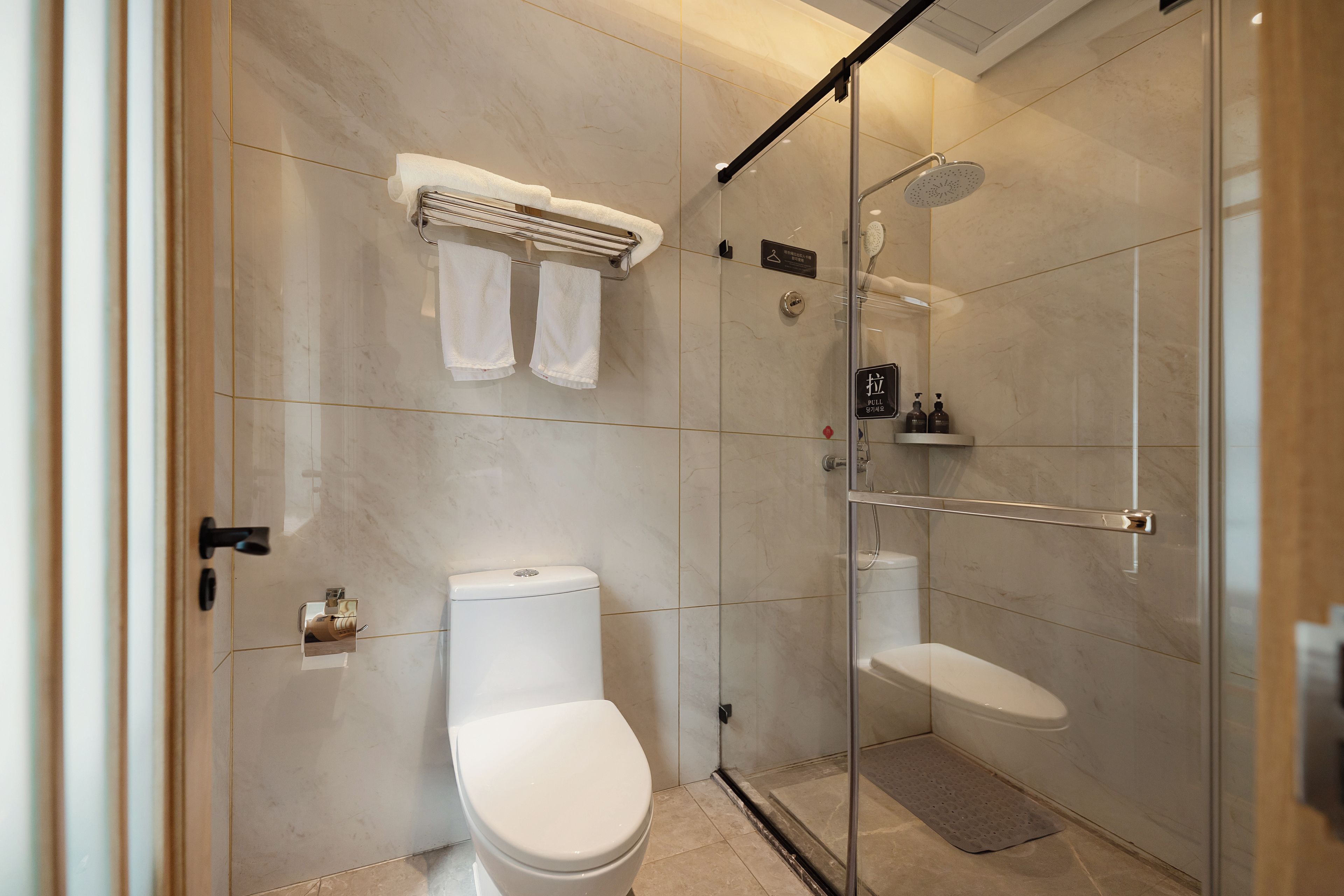 A modern bathroom with a glass-enclosed shower, a toilet, and a towel rack.
