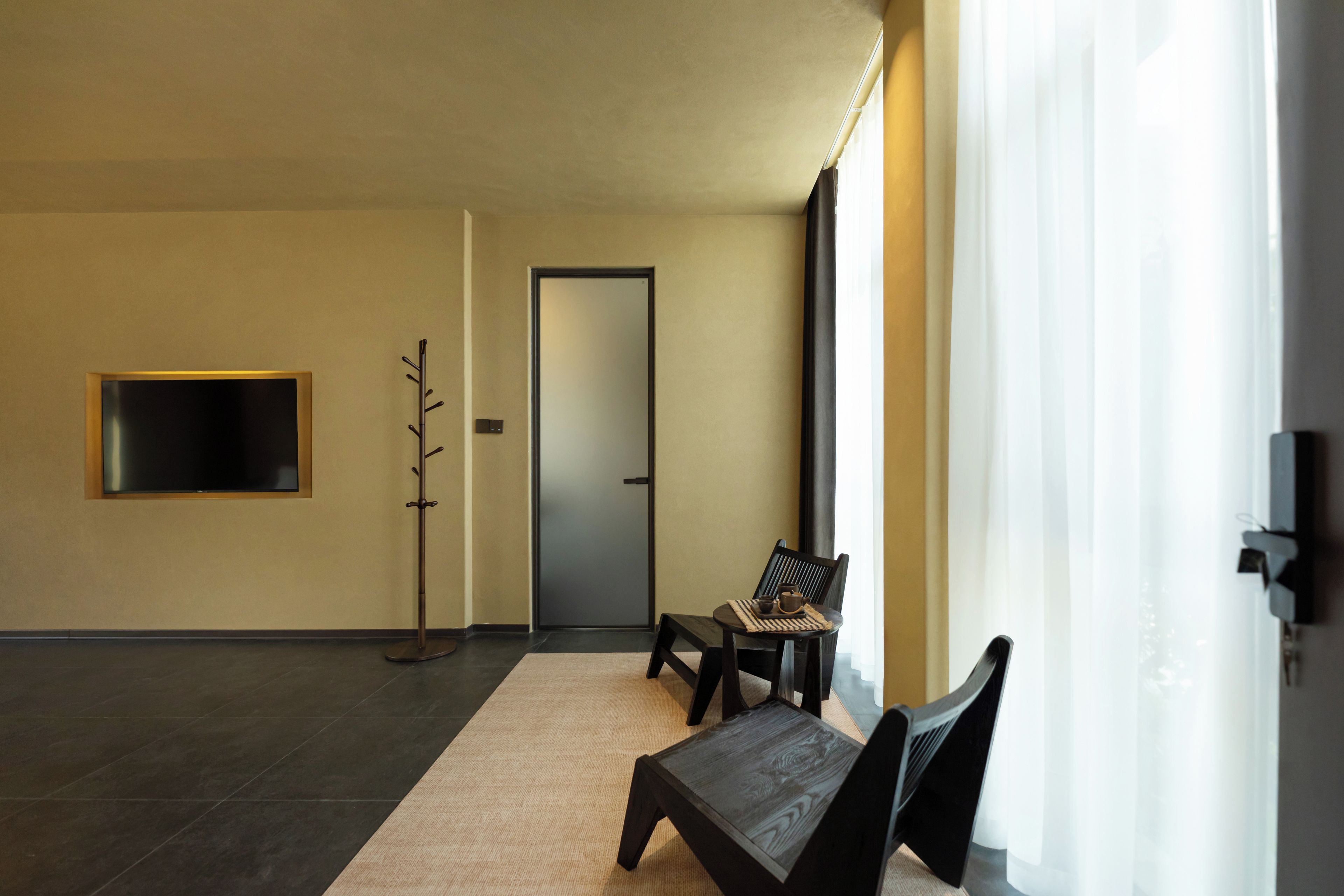 Ein modernes Interieur mit einem an der Wand befestigten Flachbildfernseher, einem Kleiderständer, einer Tür und einer Sitzecke mit einem Sessel und einem kleinen Tisch.