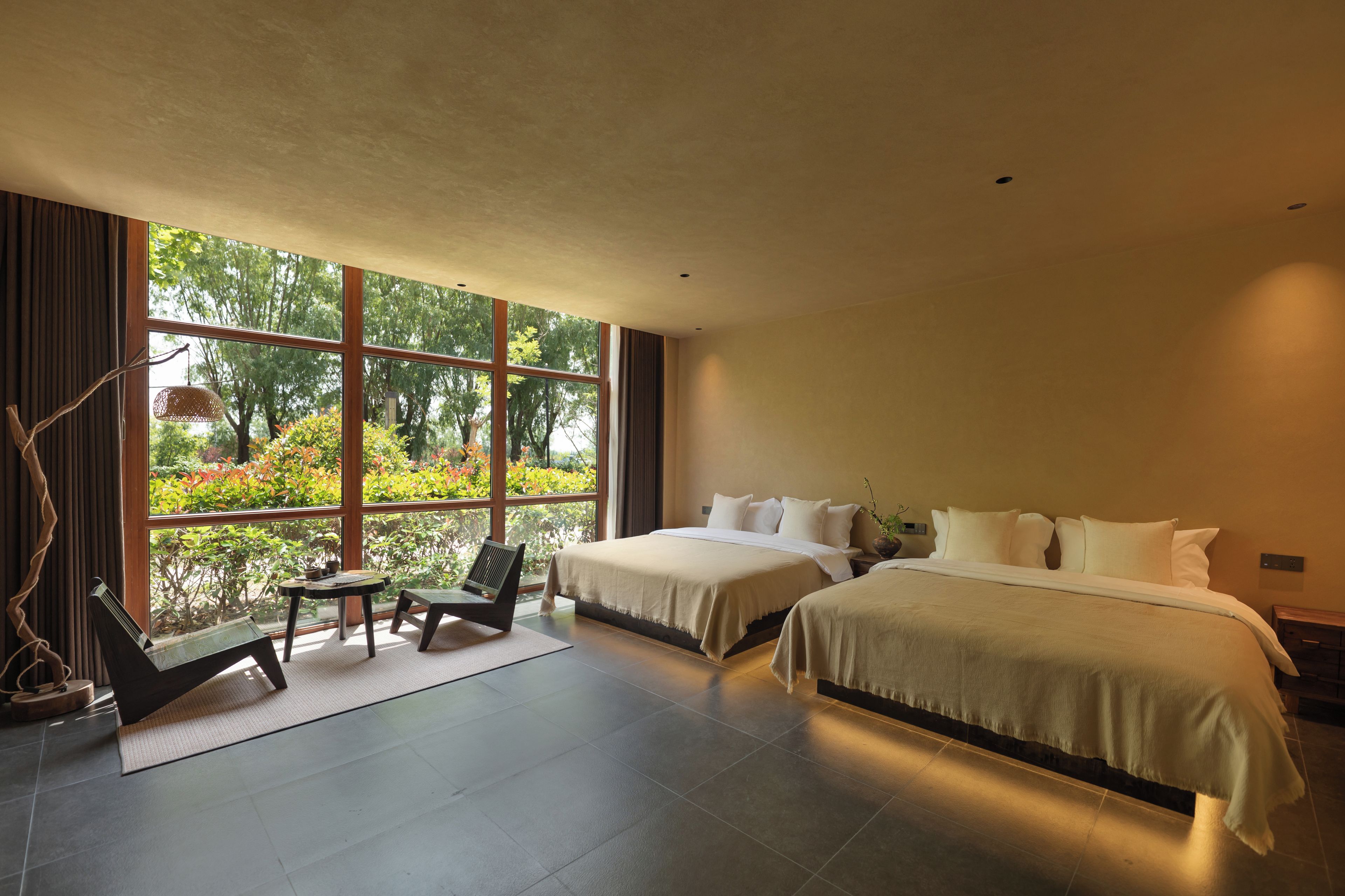 Una habitación de hotel moderna con dos camas, un ventanal grande, una mesita y una silla.
