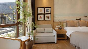 Una habitación de hotel con cama, sofá, mesita de noche, planta en maceta y un cuadro en la pared.