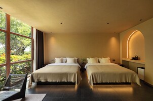 Habitación de hotel con dos camas, un ventanal grande y vista a zonas verdes.