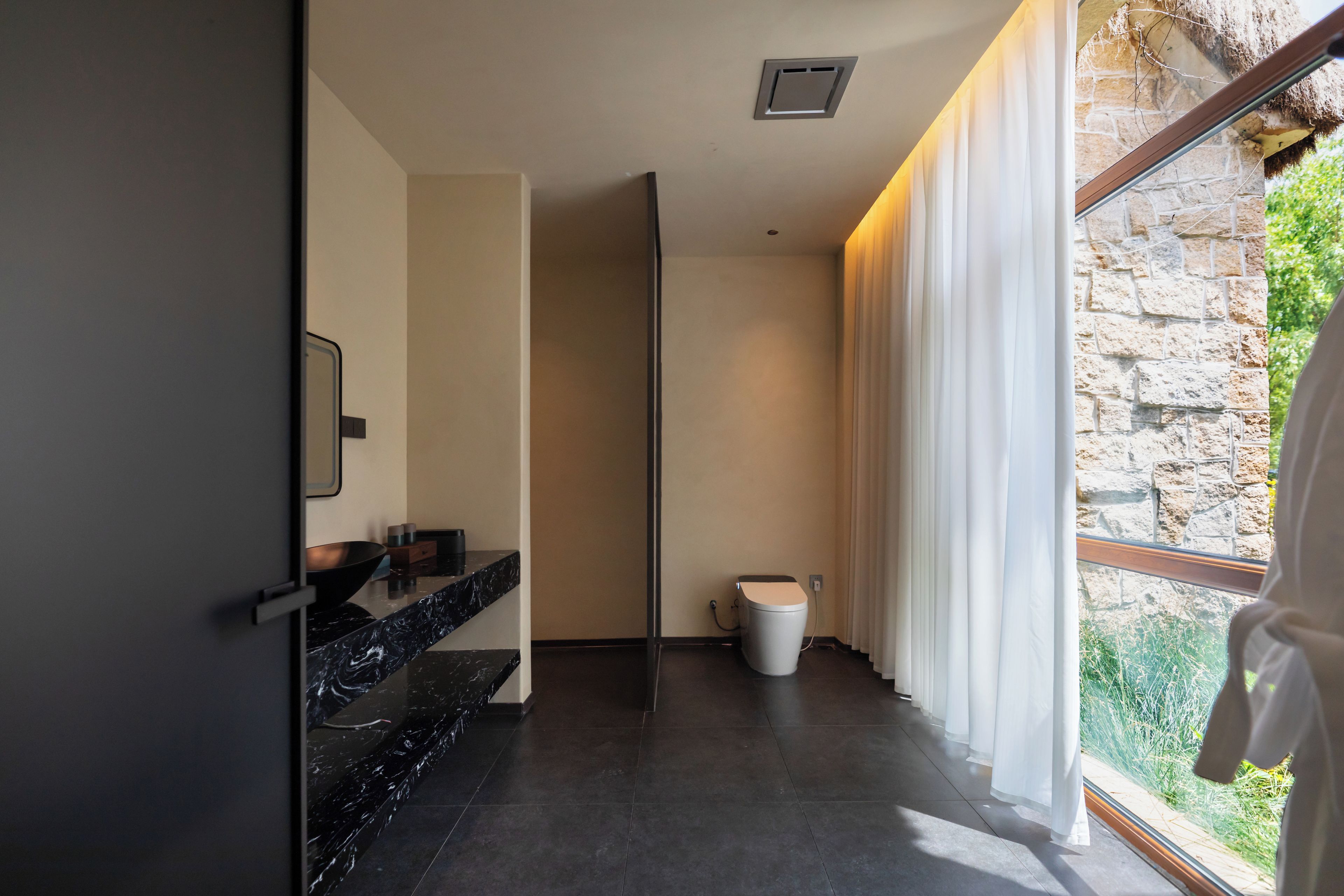 A modern bathroom with a black marble countertop, a toilet, and a window with curtains.