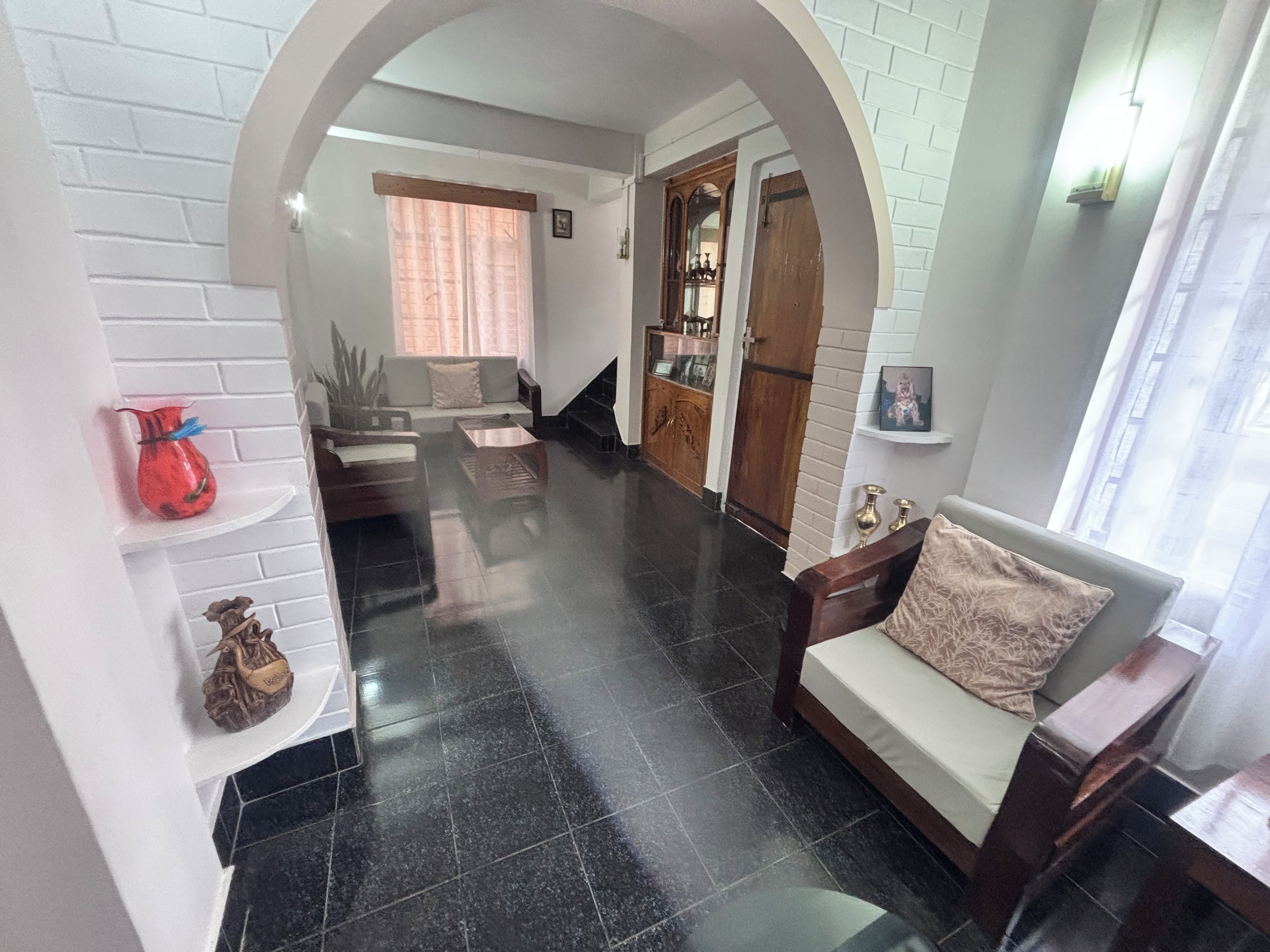 Un hall d’hôtel avec un sol carrelé de carreaux noirs, un espace salon avec des canapés et une table basse, un meuble en bois et un escalier menant à un autre niveau.