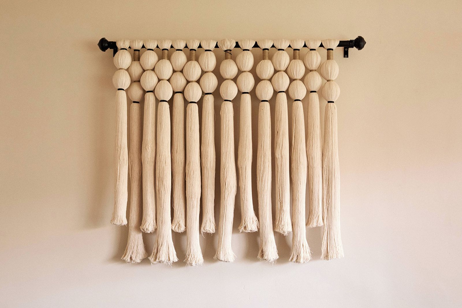 A wall-mounted macrame piece with a series of spherical and elongated elements.