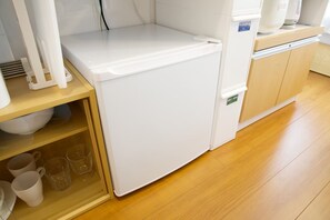 A compact kitchen with a white refrigerator, wooden cabinets, and a shelf with cups and glasses. - Lamarie Haneda 403 (Ota Ku)