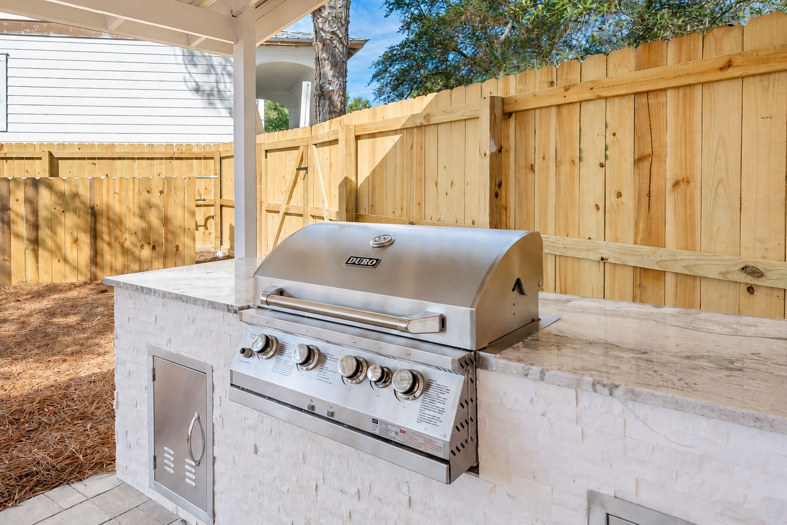 An outdoor grill with a stainless steel finish, a built-in oven, and a control panel with multiple knobs.
