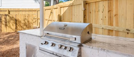 An outdoor grill with a stainless steel finish, a built-in oven, and a control panel with multiple knobs.
