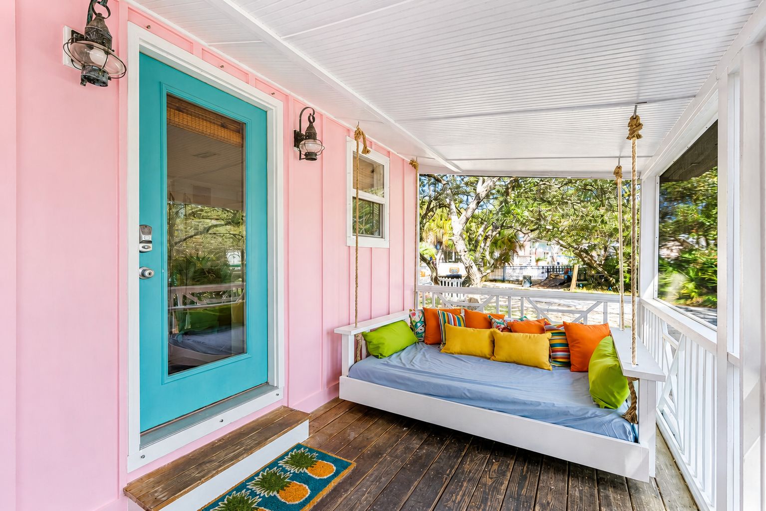 A porch with a swing seat, a door, and a view of the outdoors.