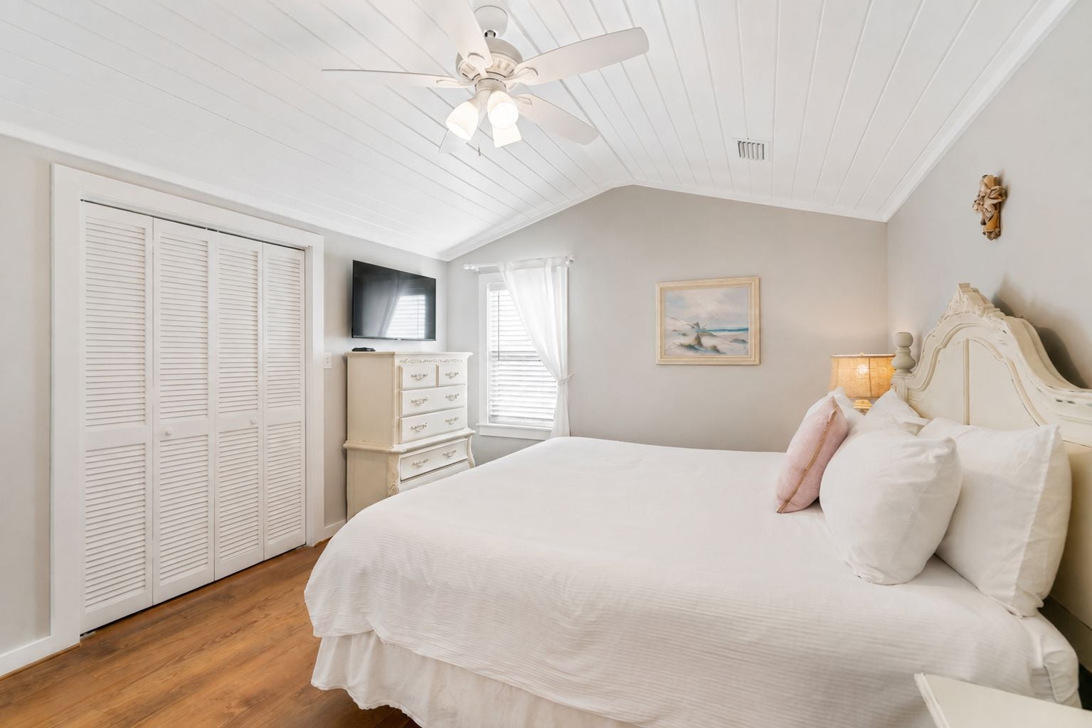 A bedroom with a bed, a dresser, a television, and a ceiling fan.