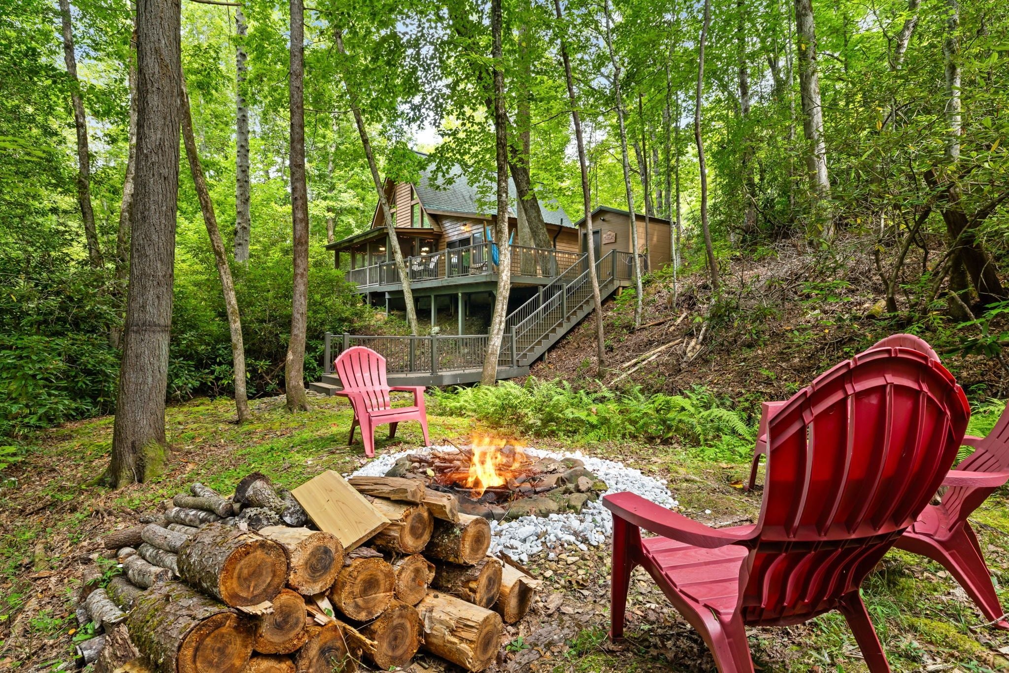 A cabin with a deck and stairs leading to a second level, surrounded by a forest.