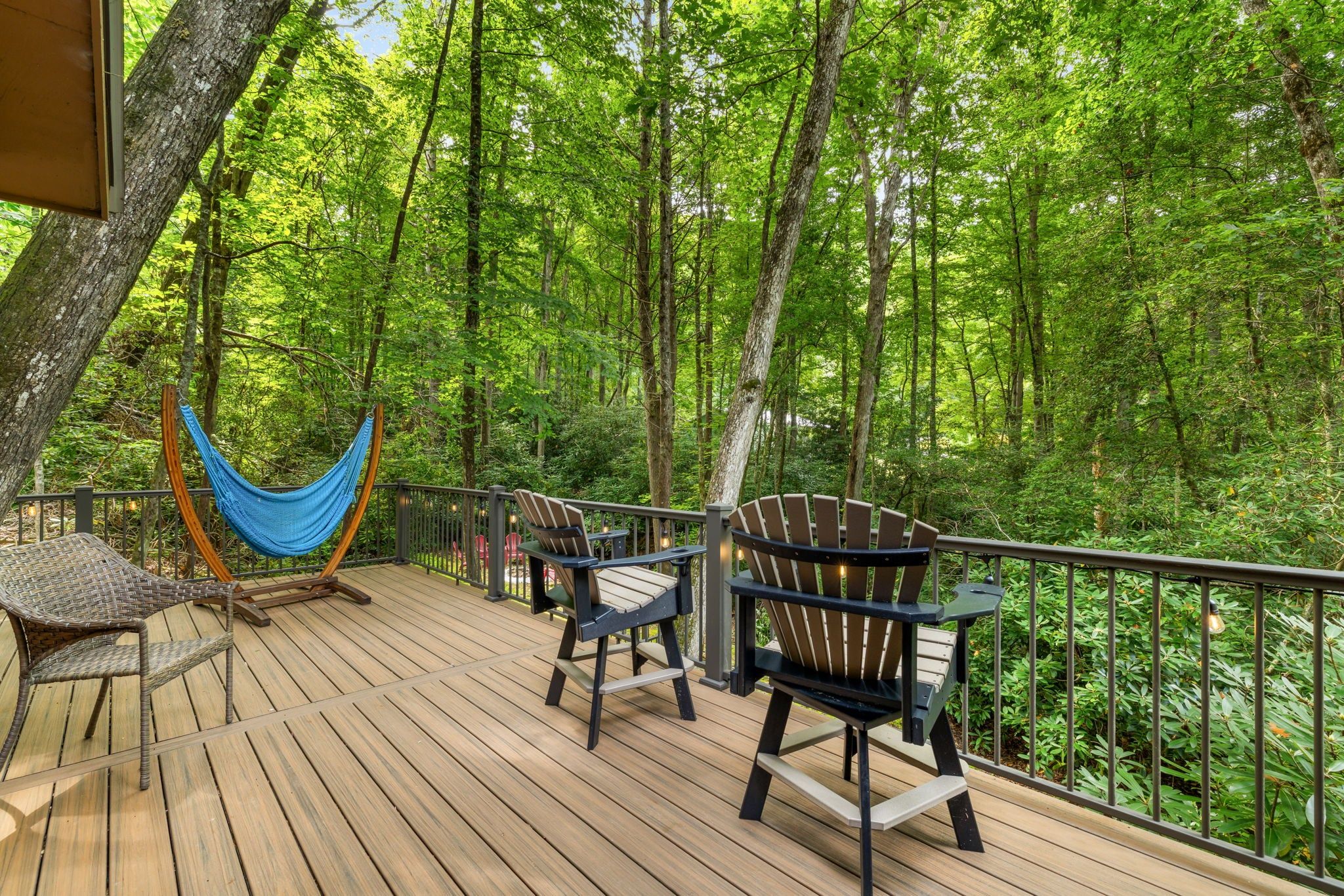 A wooden deck with outdoor furniture, including chairs and a hammock, overlooking a forested area.