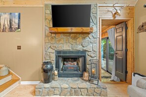 A stone fireplace with a mounted television above it, a rustic wooden door, and a painting on the wall. - Serenity by the Creek (Robbinsville)