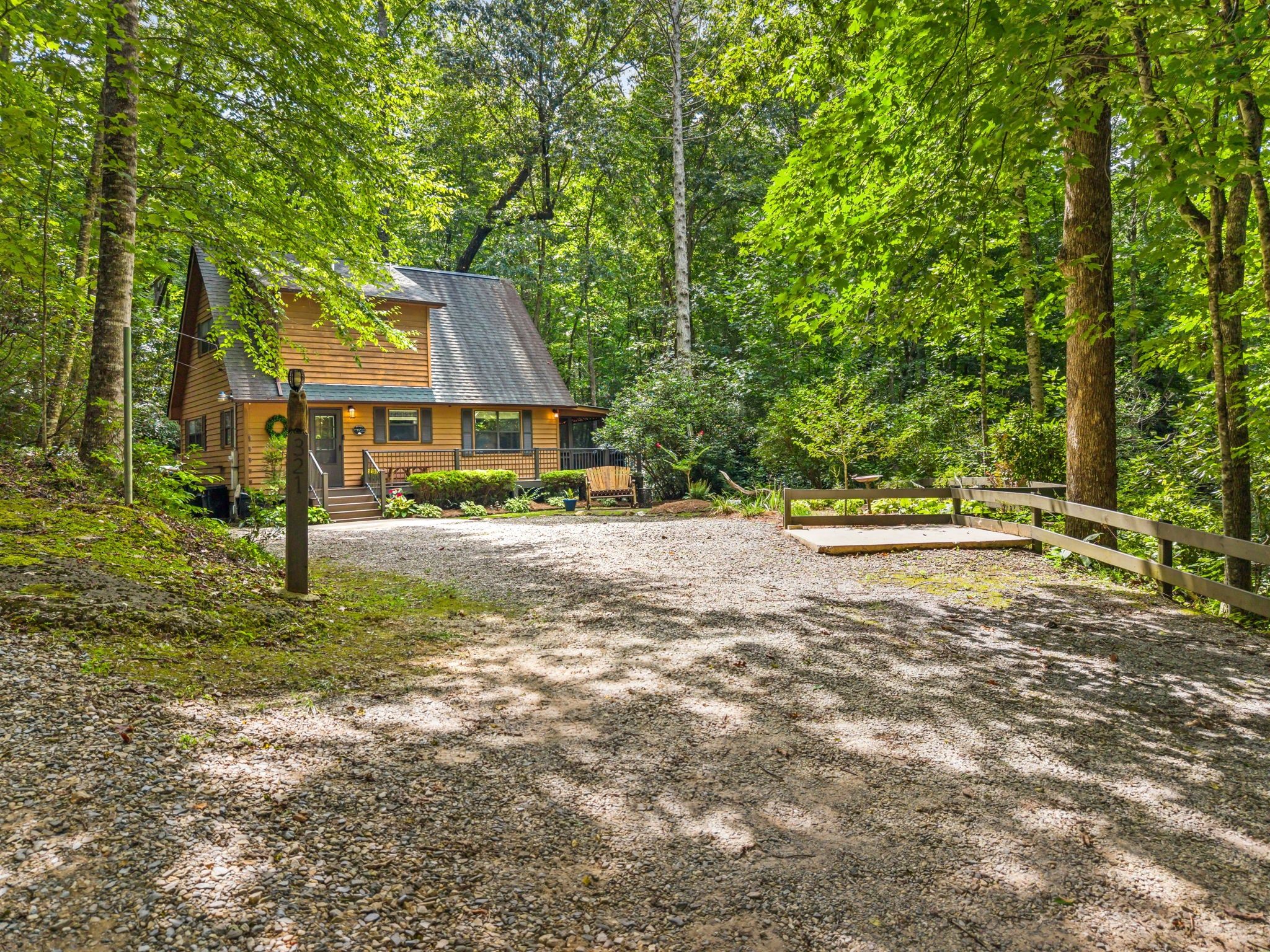 A cabin with a gravel driveway, surrounded by dense forest.