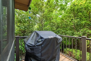A covered grill on a balcony with a metal railing and dense green foliage in the background. - Serenity by the Creek (Robbinsville)