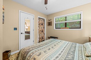 A bedroom with a bed, a window with blinds, a door, and a wall-mounted light fixture. - Serenity by the Creek (Robbinsville)