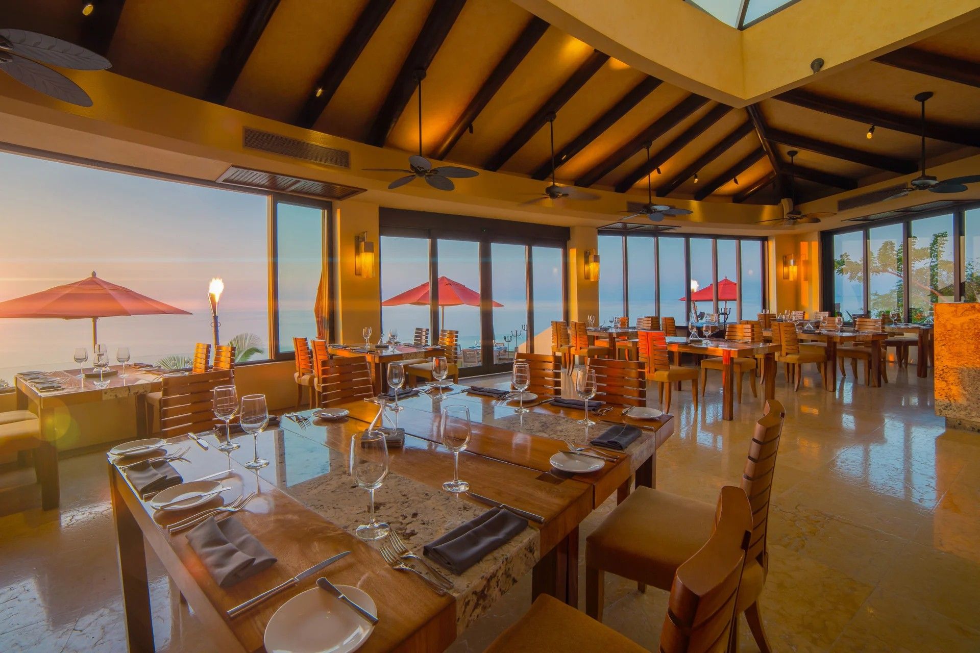 Un restaurant doté de nombreuses tables, de grandes fenêtres et de ventilateurs de plafond.