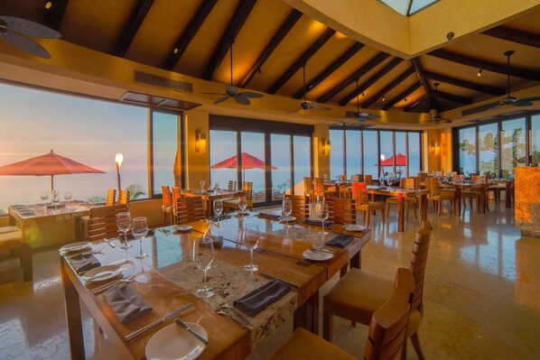 A restaurant with multiple tables, large windows, and ceiling fans.