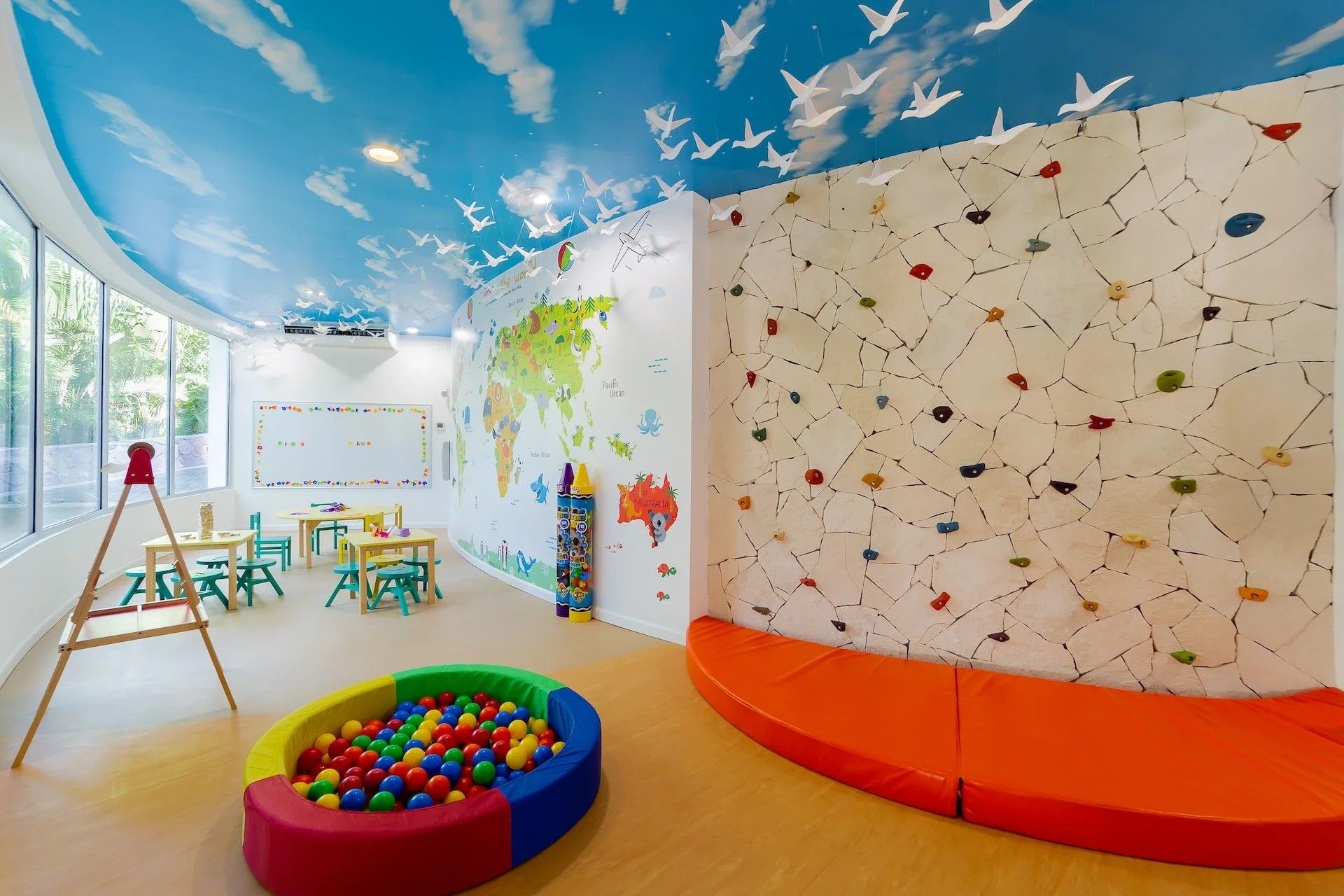 Une salle de jeux pour enfants avec une fresque représentant une carte du monde, un mur d’escalade et une piscine à balles colorée.