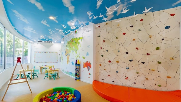 Uma sala de recreação infantil com mural de mapa mundi, parede de escalada e piscina de bolinhas coloridas.