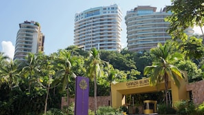 Entrada de hotel com uma placa chamativa, rodeada por palmeiras e edifícios altos modernos ao fundo.