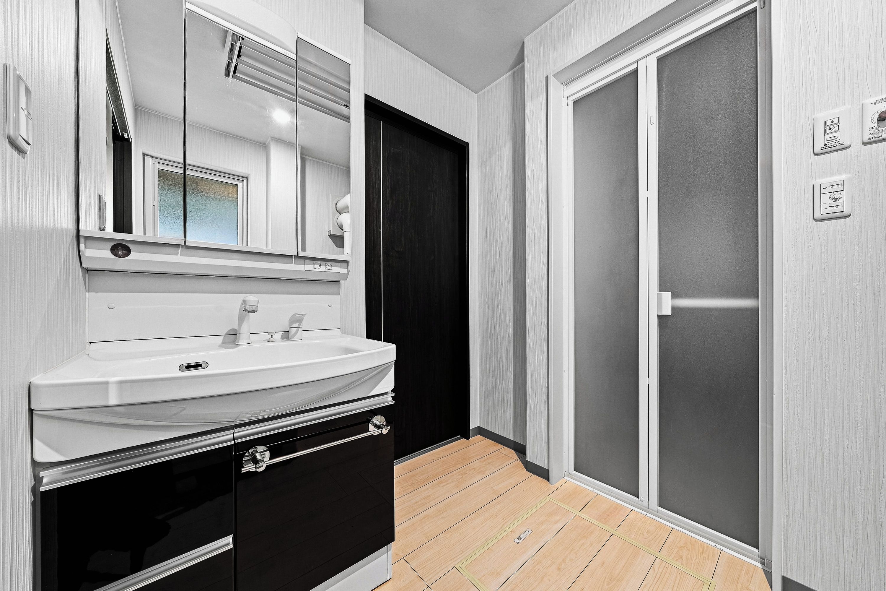 Un baño con un lavamanos blanco, un espejo, un mueble negro y una puerta corredera.
